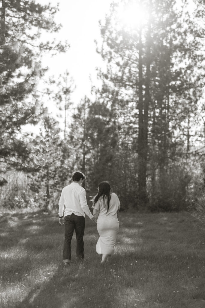 Couple walking with large pine trees behind them.